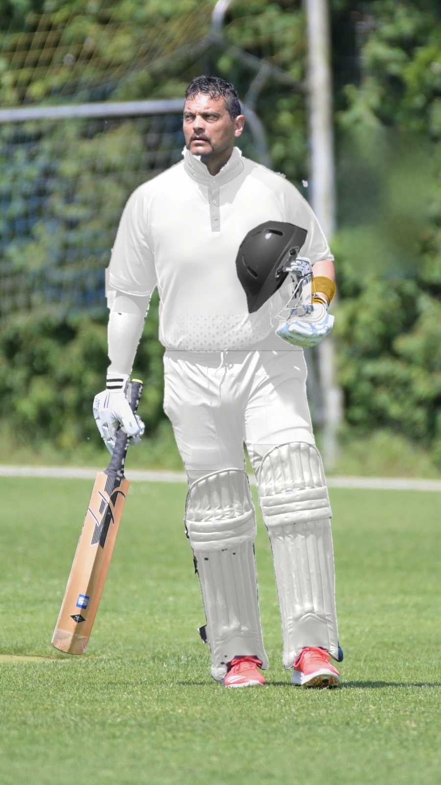 Cricketer walking in carrying a bat and helmet on an outdoor pitch
